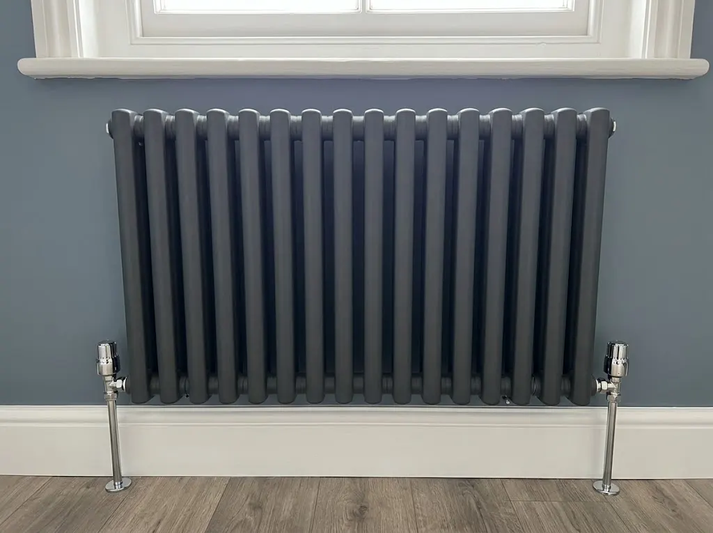 New anthracite column radiator against a painted blue-grey wall, after