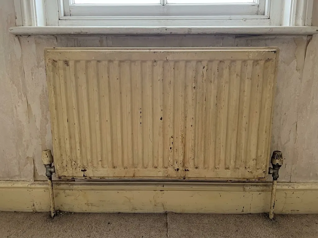 Old, stained cream radiator against peeling wall, before